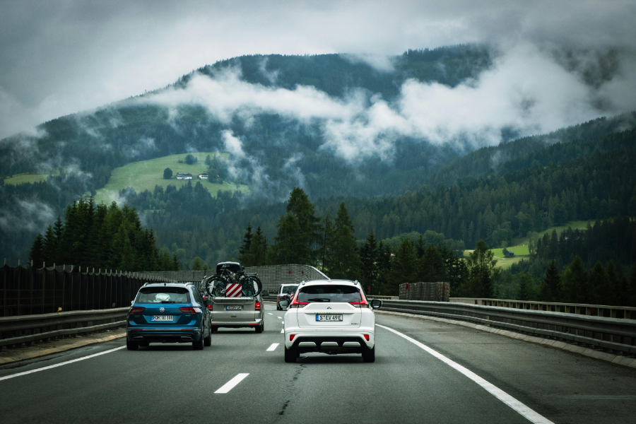 Cars travel on a highway through a misty mountain valley with green slopes and forested hills.