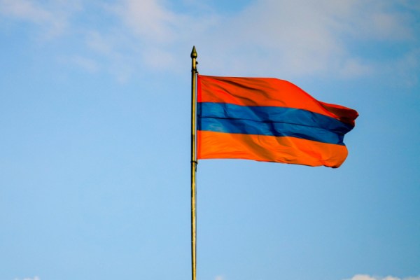Armenian national flag waving on a flagpole against a blue sky with white clouds in the background.