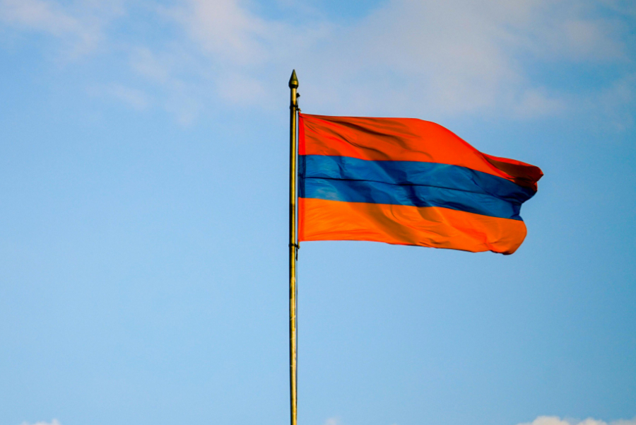 Armenian national flag waving on a flagpole against a blue sky with white clouds in the background.