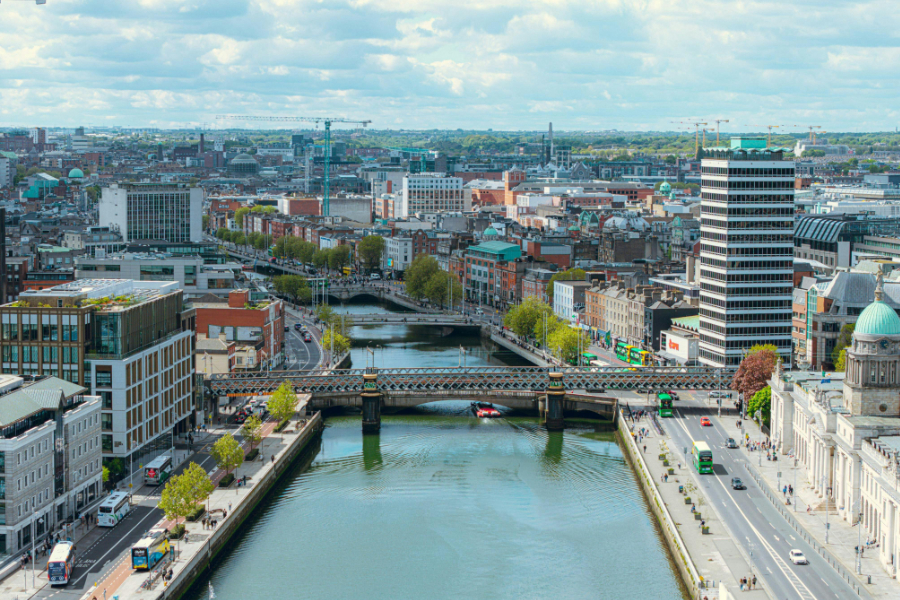 Aerial city view with a river through the center, crossing bridges, and a mix of modern and historic buildings under a partly cloudy sky.